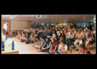 Muchos asistentes sentados en el suelo en la conferencia inaugural de Encuentros con la Ciencia